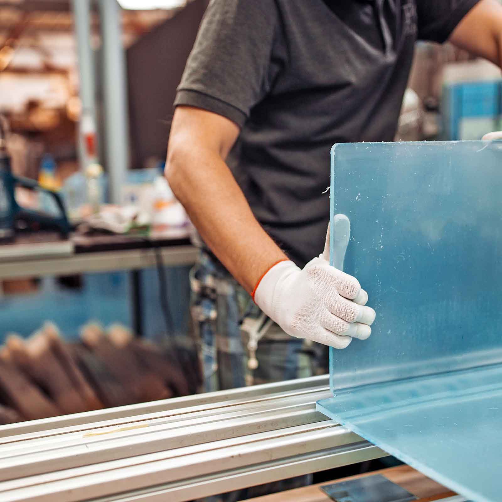 Worker handling a blue plastic sheet on a fabrication table while wearing protective gloves.